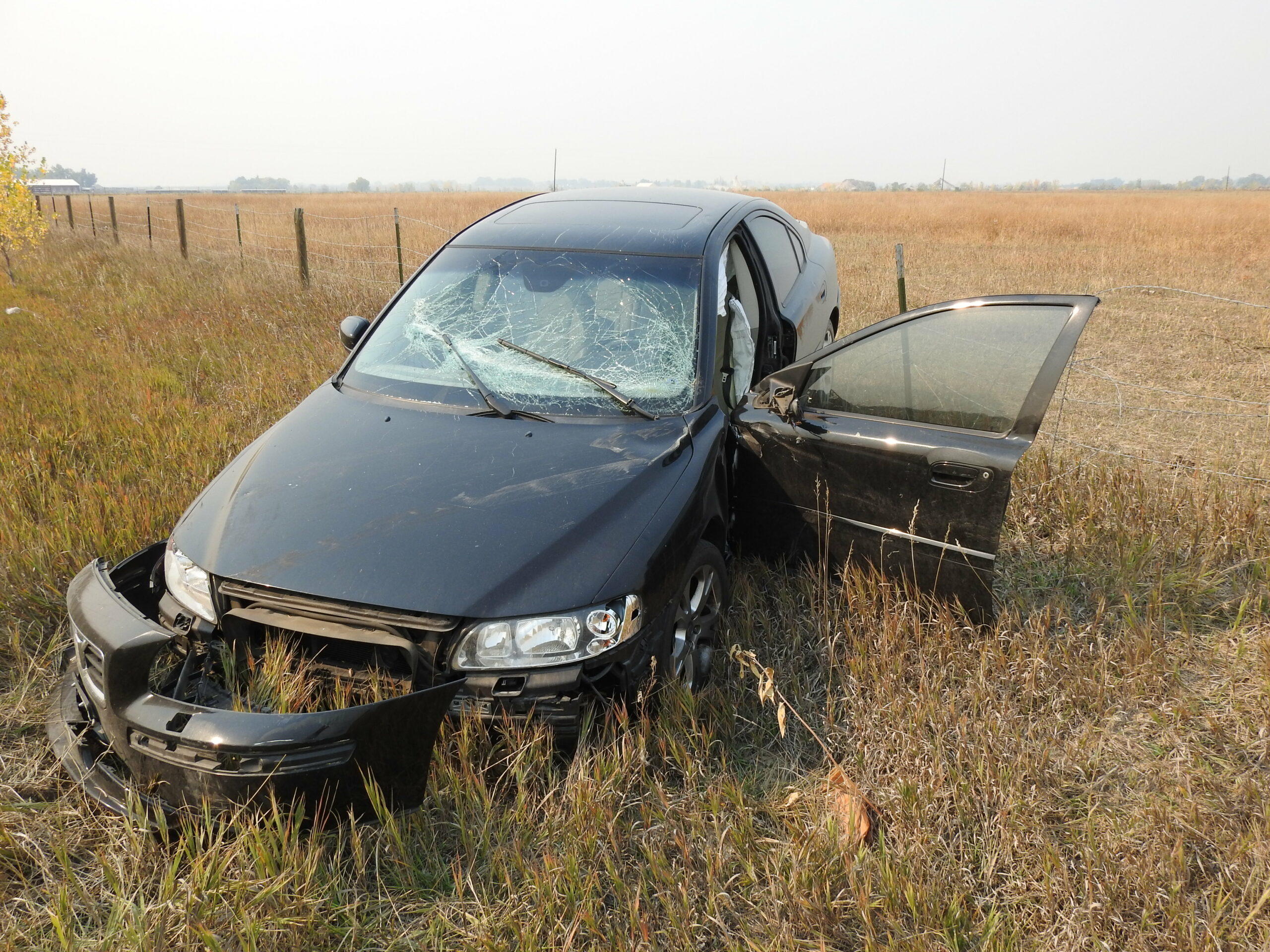 Abandonded sedan in field with broken windshield and bumper